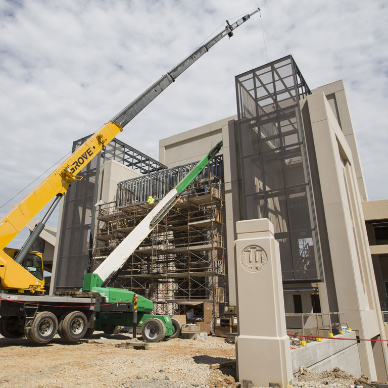 Cranes sit next to the exterior frame of a building on campus