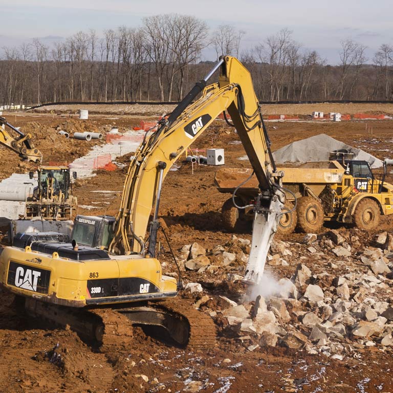 A bulldozer and dump trucks dig ground at a building site on campus