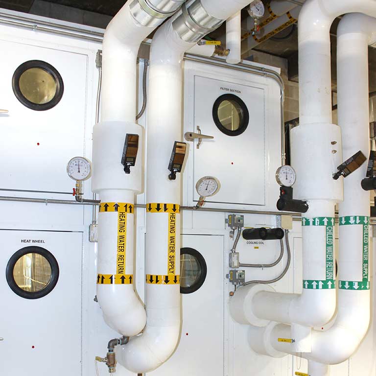 Hot and cold water pipes and values in a utility room in a building on campus