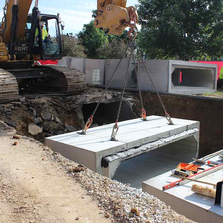Construction machinery lifts a large concrete block from the ground.